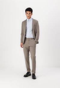 Lys brun dress med slim fit, kombinert med en lys blåstripet skjorte. Svarte lærsko fullfører antrekket. Enkelt, men moderne design.