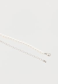 Κολιέ από λευκές πέρλες με ασημένια προέκταση αλυσίδας και κούμπωμα σε σχήμα αστακού σε λευκό φόντο.