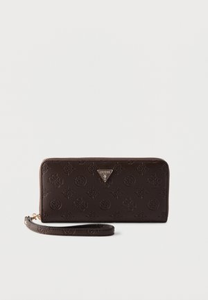 Portefeuille Guess marron foncé avec fermeture éclair tout autour, logos en relief et bracelet de poignet amovible sur un fond clair uni.
