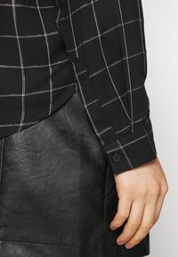 Schwarzes Hemd mit weißem Karomuster und geknöpftem Bündchen, kombiniert mit einem schwarzen Lederminirock mit glatter Textur.