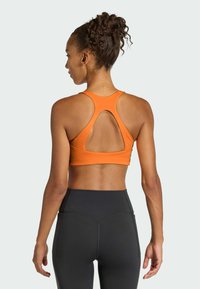 Top corto deportivo naranja con un diseño de espalda con abertura, combinado con leggings negros de cintura alta que presentan costuras en contraste.