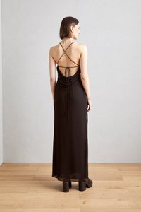 Rochie maxi neagră cu un design drapat și spate desprins. Prezintă bretele subțiri în cruce și un detaliu cu fundă în talie. Textură netedă.