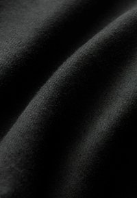 Tessuto nero che mostra una consistenza morbida con pieghe, caratterizzato da una finitura liscia e sottili variazioni di tonalità sulla superficie.