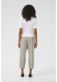 White fitted short-sleeve top paired with beige striped tapered pants. Pants feature an elastic cuff at the hem and black slip-on shoes.