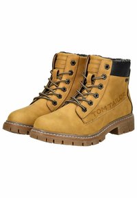 Bottines en cuir tan avec des accents noirs, présentant un extérieur texturé, des lacets robustes et une semelle solide. Marque "TOM TAILOR" visible.