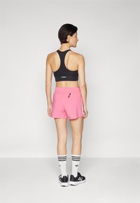 Sutien sport negru, pantaloni scurți roz, dungi laterale albe, adidași negri cu tălpi albe și șosete cu dungi negre și albe. Texturi netede.
