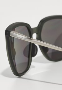 Solsikker med en matt svart ramme, grå linser og en metallisk sølv arm. Har "Oakley"-logoen på armen.