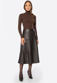 Bruine coltrui met geribbelde textuur, gecombineerd met een donker lederen A-lijn rok met paneelstiksels en een uitlopende zoom. Zwarte hakken.
