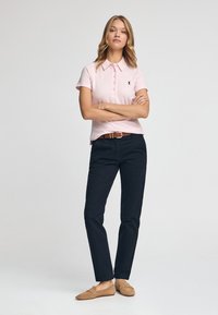 Camisa polo rosa claro con cinco botones y un pequeño logo, combinada con pantalones rectos azul marino y mocasines de ante marrón.