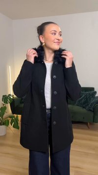 Čierny kabát s golierom z umelého kožušina, zapínaný na gombíky, s dvoma bočnými vreckami a strihaný na mieru. Nosí sa cez svetlosivý top a je doplnený tmavými džínsami.