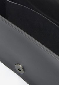 Portafoglio in pelle nera con una superficie liscia, dotato di una chiusura magnetica e di un sottile dettaglio di cucitura lungo i bordi.