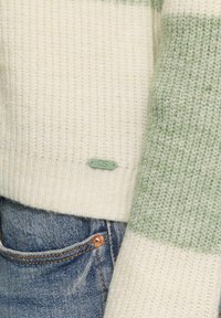 Gebreide trui met lichtgroene en crèmekleurige strepen, ribbeltekstuur en een klein QS-label op de zoom, gecombineerd met blauwe denim jeans.