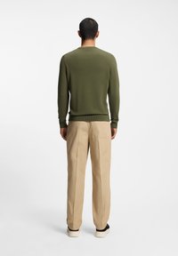 Grøn strikket trøje med rund hals, kombineret med beige bukser med lige ben. Outfit'et har en glat tekstur og afslappet pasform.