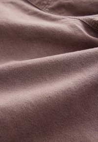 Textilstoff in einem sanften, gedämpften Mauve-Ton, mit einer glatten Textur, sichtbaren gerippten Mustern und sanften Drapierungen.