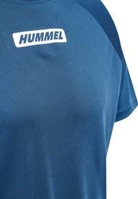 Blå tränings t-shirt tillverkad av andningsbart material, med korta ärmar, rund halsringning och en vit "HUMMEL"-logotyp på bröstet.