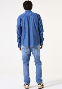 Blauw denim shirt met lange mouwen en knoopdetails, gecombineerd met lichtblauwe denim jeans en bruine veterschoenen.