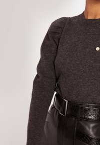 Suéter gris oscuro con textura acanalada, que presenta pliegues en los hombros y un acento de perlas, combinado con un cinturón de cuero negro que muestra un acabado brillante y texturizado.