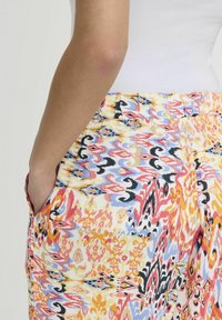 Barevné kalhoty se vzorem, které mají živý design se žlutými, růžovými, modrými a černými akcenty. Obsahují kapsy a texturovanou látku.