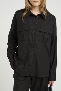 Camicia nera con bottoni realizzata in tessuto texturizzato, dotata di due tasche sul petto e colletto. Maniche lunghe con orli a polsino.