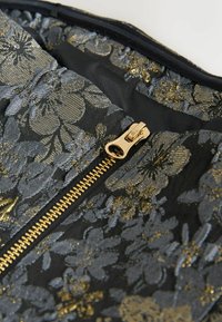 Fekete alapú szövet, metallic arany és szürke virágmintával. Arany színű cipzárral rendelkezik, sima húzófüllel. A belső bélés fekete.
