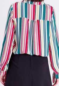 Blouse rayée multicolore avec des lignes verticales en rouge, rose, vert, bleu sarcelle et noir. Manches longues et un empiècement au dos.