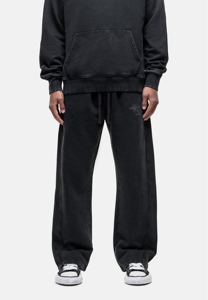 Zwarte oversized hoodie met een voorzak, gecombineerd met losse zwarte joggingbroek met een elastische tailleband en logo-detail.