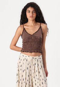 Top court ajusté marron, avec des volants, des bretelles spaghetti ajustables et un design smocké. Associé à une jupe crème avec un motif de diamants noirs.