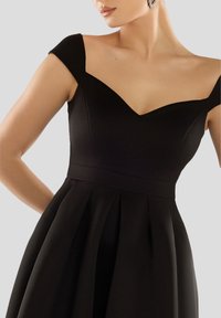 Zwarte jurk met een aansluitende corsage, een V-halslijn en kapmouwen, een vloeiende geplooide rok en een gladde, gestructureerde stof.