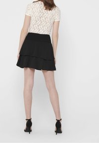 Black tiered skirt with a smocked waistband, paired with a white lace top. The outfit features short sleeves and a fitted silhouette.