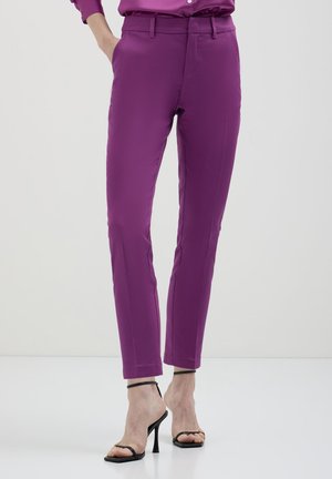 Pantaloni a sigaretta in tessuto viola vivace, caratterizzati da una texture liscia e una leggera lucentezza, abbinati a sandali neri con tacco alto.