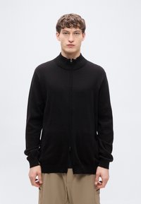 Μαύρο ζακέτα με φερμουάρ, κατασκευασμένο από απαλό ύφασμα, διαθέτει ψηλό γιακά, μακριά μανίκια και πλαϊνές τσέπες. Λεία υφή με εφαρμοστή σχεδίαση.