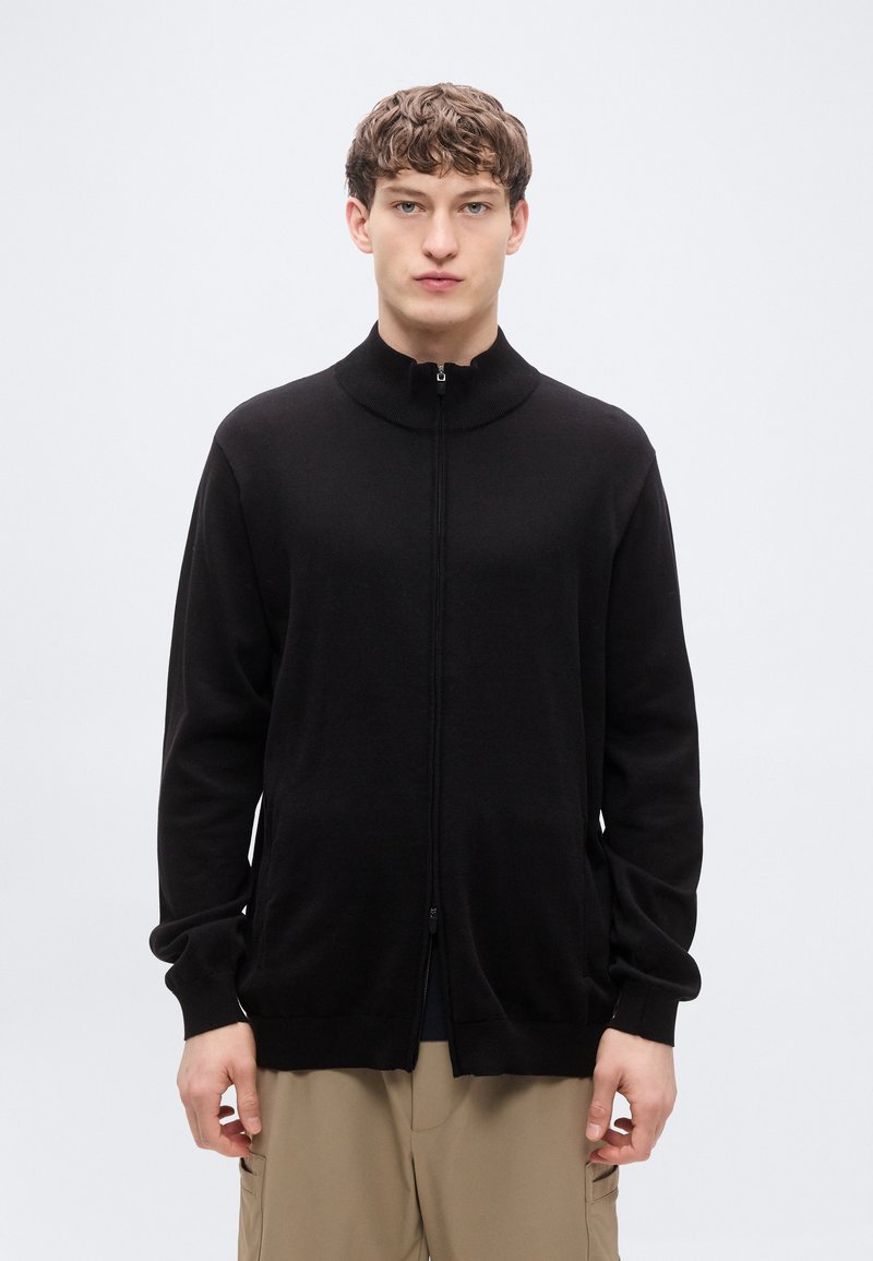 Μαύρο ζακέτα με φερμουάρ, κατασκευασμένο από απαλό ύφασμα, διαθέτει ψηλό γιακά, μακριά μανίκια και πλαϊνές τσέπες. Λεία υφή με εφαρμοστή σχεδίαση.