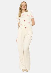 Beige knit sweater with short sleeves featuring pink flower appliqués, paired with light cream wide-leg pants and light-colored shoes.