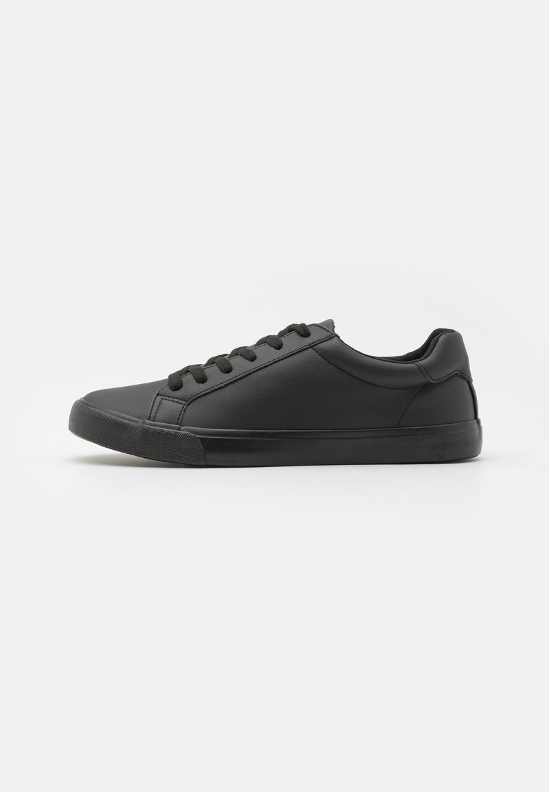 Zapatilla de cuero sintético negro con puntera redondeada, suela gruesa y cordones planos negros. Presenta una textura suave y un diseño minimalista.