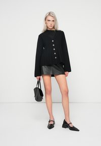 Cardigan negru din tricot cu un design evazat, având cinci butoane metalice. Asortat cu o fustă mini din piele ecologică neagră și balerini cu vârful ascuțit.