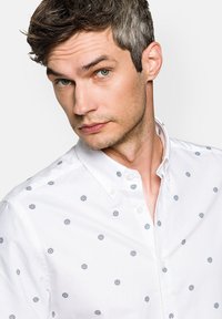 Biała koszula z guzikami, ozdobiona małymi niebieskimi kwiatowymi wzorami, z wykładanym kołnierzykiem i gładką bawełnianą fakturą.