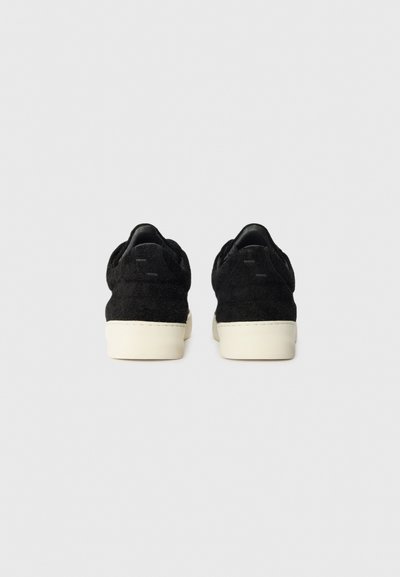 Sorte semskede sneakers med teksturert overdel, kremfarget gummisåle, avrundet form og minimal merkevare på hælen.