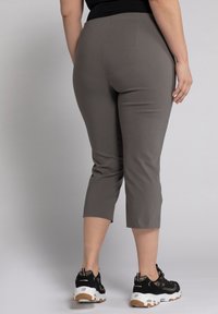 Grå beskårne bukser med en glat tekstur og skræddersyet pasform, der har en mid-rise talje og en sideslids i kanten, parret med sorte sneakers.