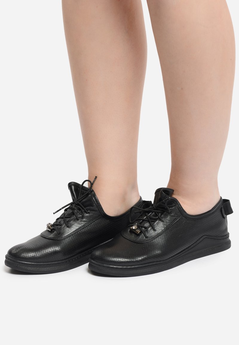 Schwarze, durchbrochene Lederschuhe mit Schnürdesign, einem strukturierten Finish und einem Zugtab am Fersenbereich für einfaches An- und Ausziehen.