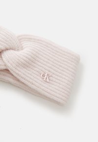 Diadema de punto acanalado rosa con un diseño anudado y un pequeño logo en relieve. Textura suave con un ajuste ceñido.
