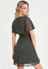 Schwarzes Kleid mit kurzen, durchsichtigen Ärmeln, elastischem Bund und floralem Muster in Grün, Rot und Weiß. Der Saum sitzt über dem Knie.