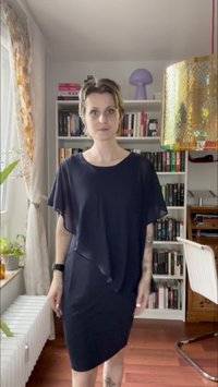 Schwarzes Kleid mit einem fließenden, geschichteten Oberteil und einem figurbetonten unteren Teil, aus leichtem Stoff mit glatter Textur. Kurze Ärmel und knielang.