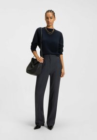 Marineblauer Pullover und gestreifte Hosen, dazu eine schwarze Leder-Schultertasche und spitze Absätze. Schlichtes Design mit strukturierter Passform und Texturen.
