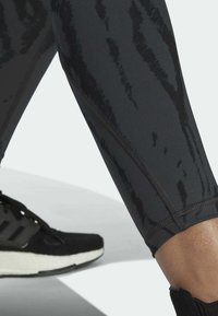 Zwarte sportlegging met een textuurpatroon, voorzien van een strakke pasvorm en platte naden. Gecombineerd met een zwarte hardloopschoen die onderaan zichtbaar is.