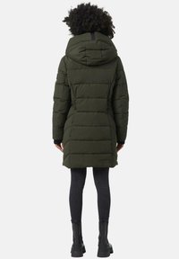 Grøn pufferjakke med hætte, der har quiltet design, justerbar talje og sidelommer, parret med sorte skinny jeans og støvler.