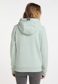 Mikina s kapucí ve světlé mátově zelené barvě, s jemnou texturou, žebrovanými manžetami a lemem, a malou nášivkou loga na zadní straně.