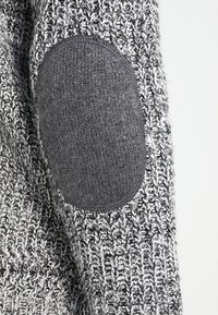 Pull en tricot présentant un motif texturé gris avec des coudières gris foncé contrastantes, améliorant la durabilité et le style.