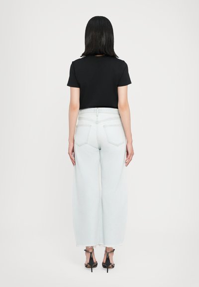 Μαύρο πουκάμισο με κοντά μανίκια συνδυασμένο με ανοιχτό μπλε τζιν παντελόνι με φαρδύ πόδι και φθαρμένο τελείωμα. Μαύρα πέδιλα με λουράκια ολοκληρώνουν την εμφάνιση.