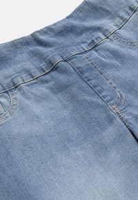 Lys blå denimjeans close-up, der viser elastisk taljebånd, syninger ved forlommerne og stoftekstur.