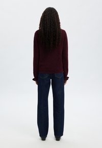 Bordo pulover z dolgimi rokavi in nabranimi manšetami, kombiniran s temno modrimi širokimi jeans hlačami. Gladek tekstura, minimalističen dizajn.